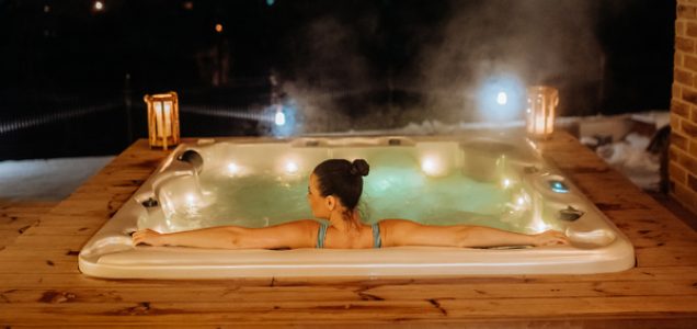 Rear view of young woman enjoying outdoor bathtub in her terrace during a cold winter evening.